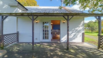 A white building with a covered porch, a door with glass panels, and a small table with chairs inside.
