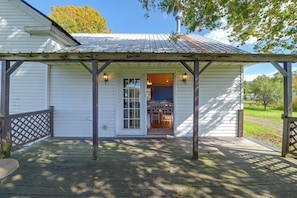 A white building with a covered porch, a door with glass panels, and a small table with chairs inside.