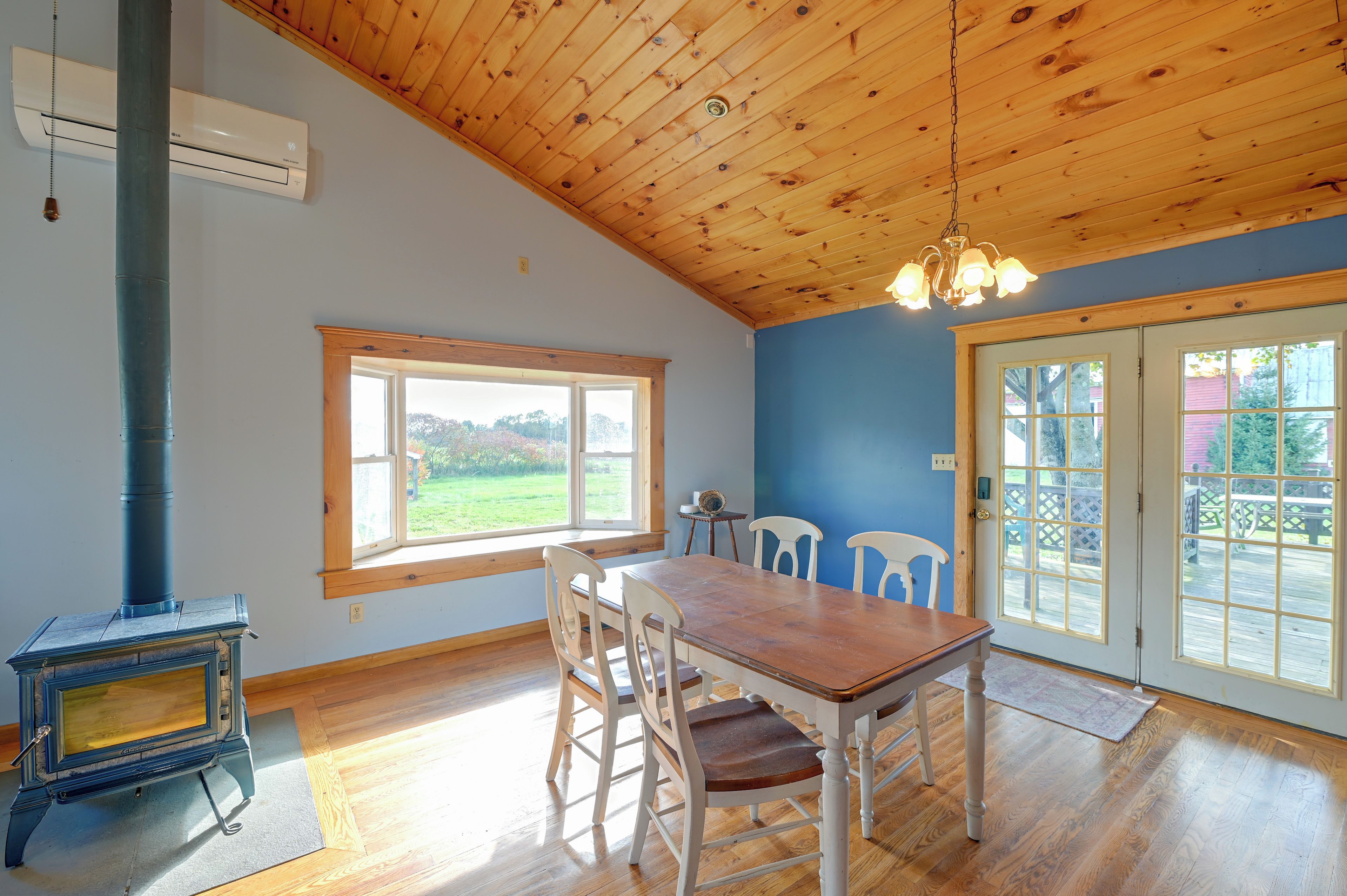 Une pièce avec un plafond en bois, une grande fenêtre, une table à manger avec des chaises et un poêle à bois.