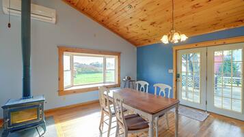 Une pièce avec un plafond en bois, une grande fenêtre, une table à manger avec des chaises et un poêle à bois.