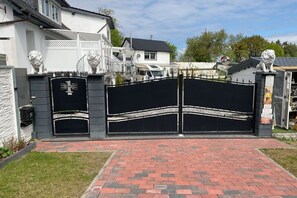 A gated entrance with a black gate, a white house with a grey roof, and a statue of a lion. - Bungalow in Rheinsberg with swimming pool (Rheinsberg)