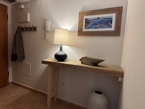En gang med en træbænk, en lampe, et indrammet billede, et knagered og en skraldespand.