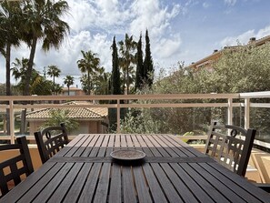 A wooden table with chairs on a balcony, overlooking a garden with palm trees and a building with a tiled roof. - L'Oneta Mediterranean charm by the sea (Badia de Xàbia)