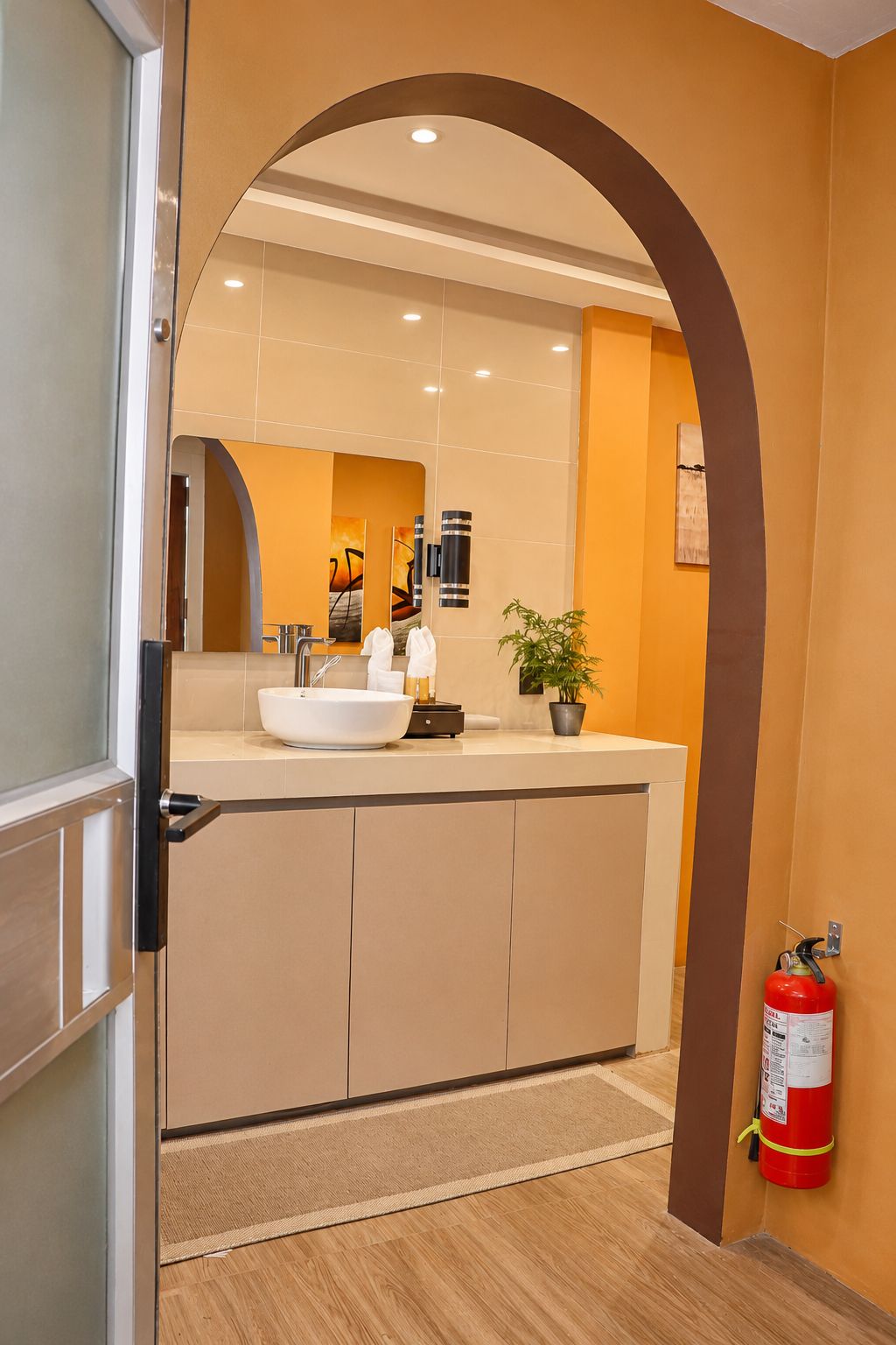 A modern bathroom with a large sink, mirror, and a fire extinguisher mounted on the wall.
