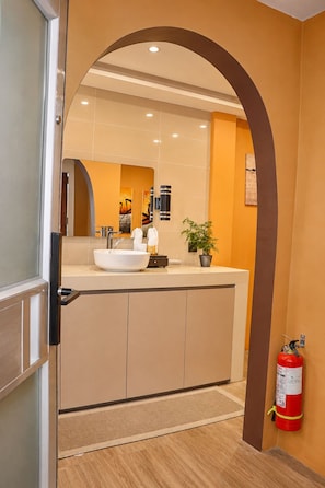 A modern bathroom with a large sink, mirror, and a fire extinguisher mounted on the wall.