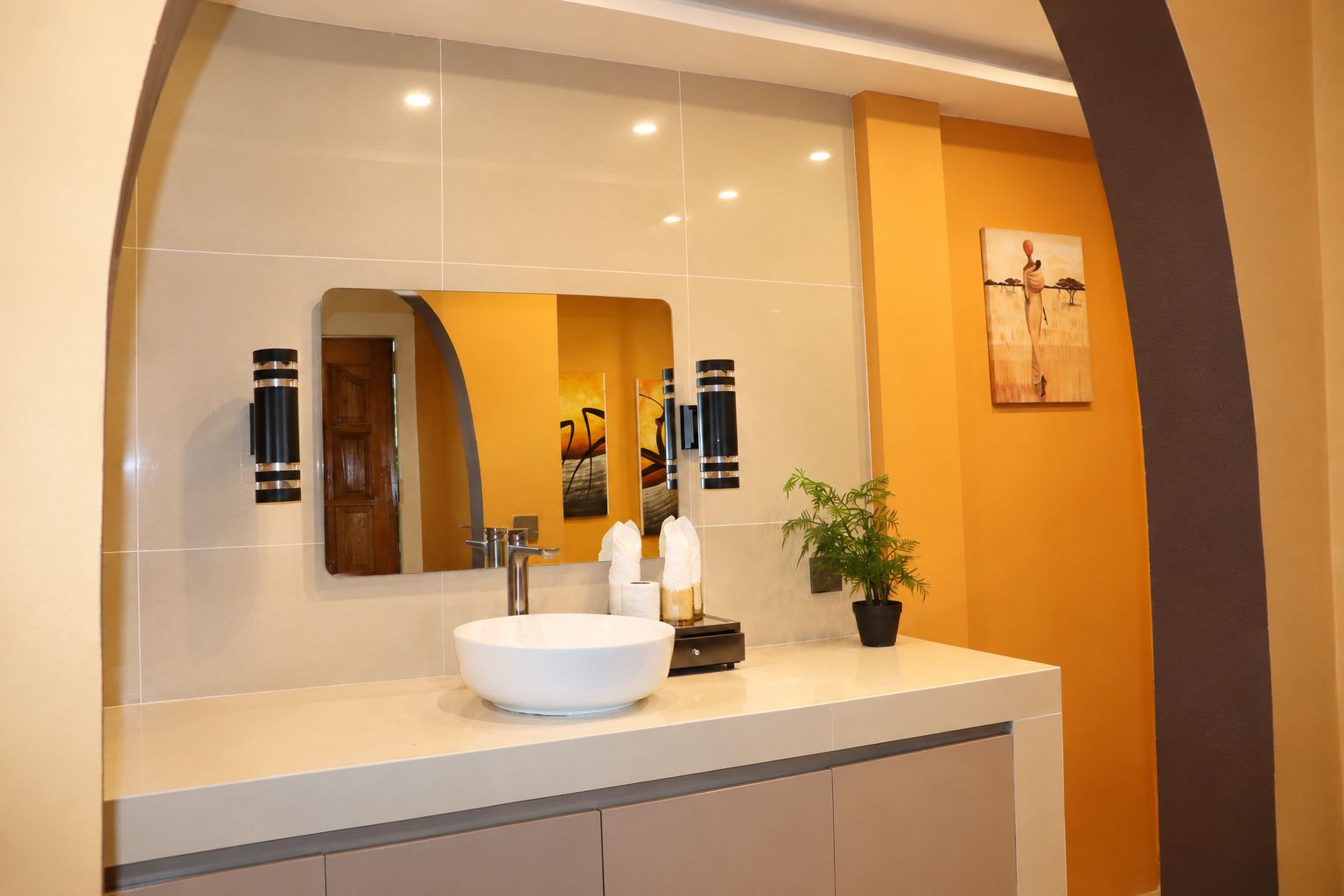 A modern bathroom with a large mirror, a white sink, and a potted plant.