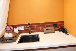 A kitchen with a sink, a tissue box, a power outlet, and a basket with cups and a vase of flowers. - Romantic Love Nest Dome Retreat at Pebble Walk Beach Resort (Romblon)