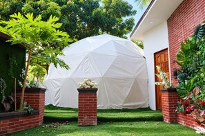 Uma tenda branca num jardim com um muro de tijolos e uma porta de madeira.