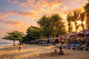 A beach with sun loungers and umbrellas, a person running with a surfboard, and a child playing with sand. - Your Coastal Getaway Just minutes from Jomtien Beach (Pattaya City)
