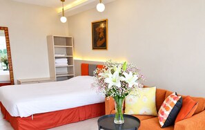 A hotel room with a bed, a bedside table, a sofa, a small table, a vase with flowers, a bookshelf, and a painting on the wall. - Near Beach Condo with Pool Access in Pattaya City (Pattaya City)