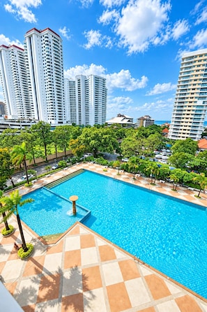 A swimming pool with a tiled deck, surrounded by palm trees and buildings in the background. - Near Beach Condo with Pool Access in Pattaya City (Pattaya City)