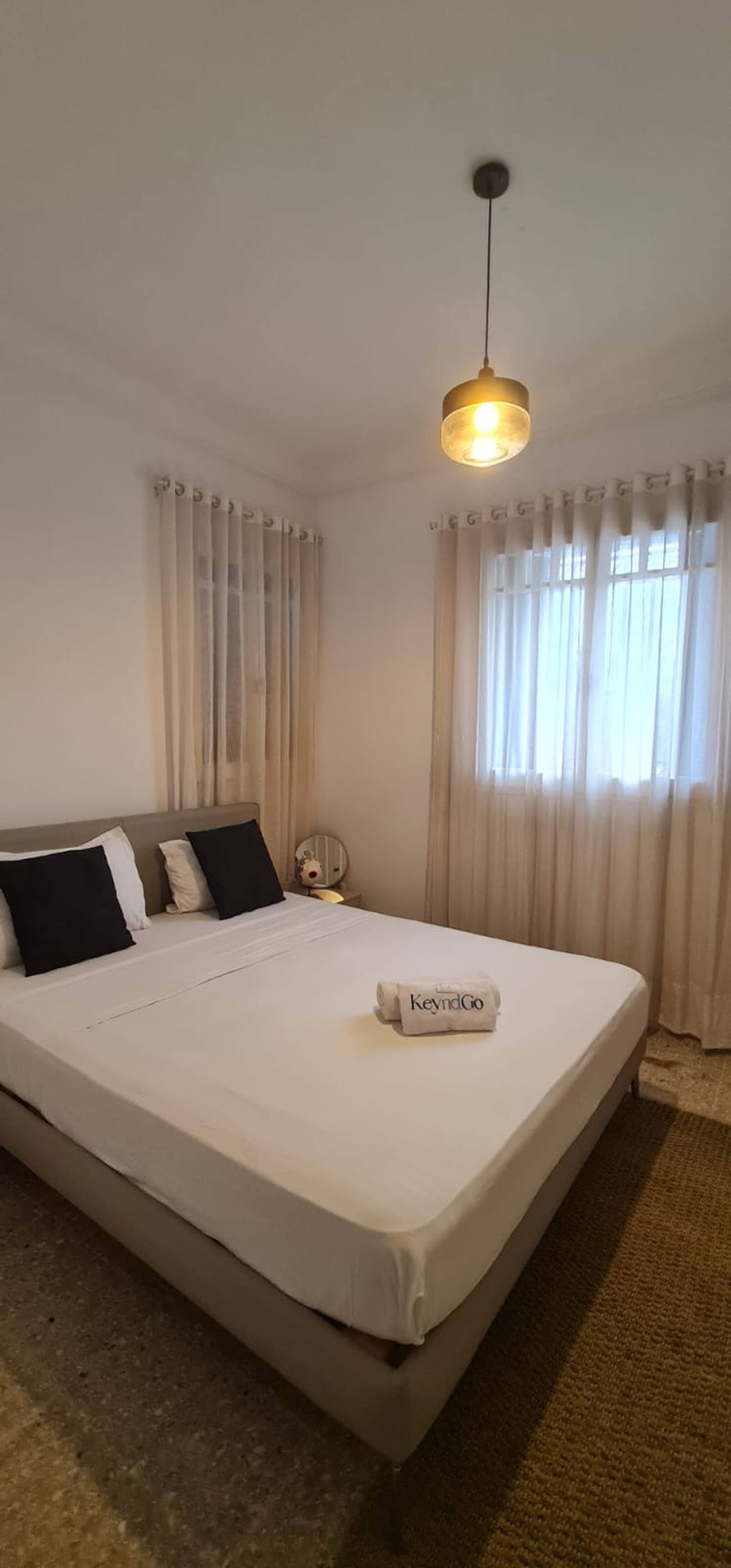 Hotellihuone, jossa on sänky, pyöreä pöytä ja riippuvalaisin.