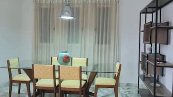 Un coin repas avec une table et des chaises en verre, un luminaire suspendu, un sol en marbre et une bibliothèque.