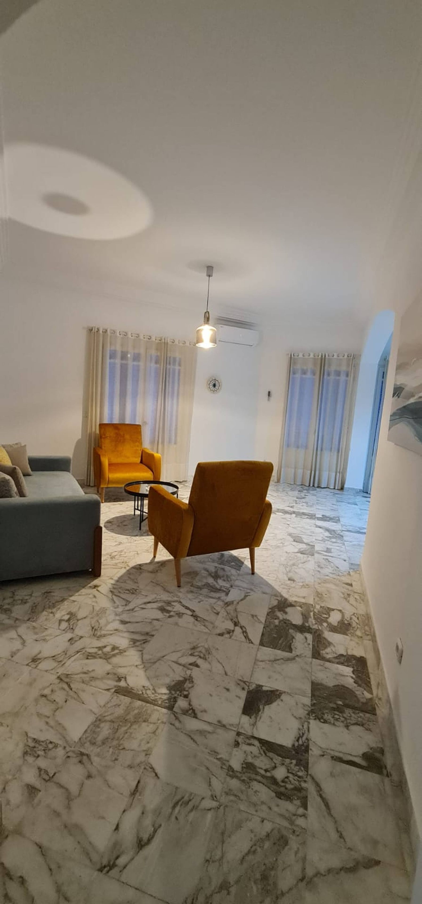 A modern living room with a sofa, armchairs, a coffee table, and a marble floor.