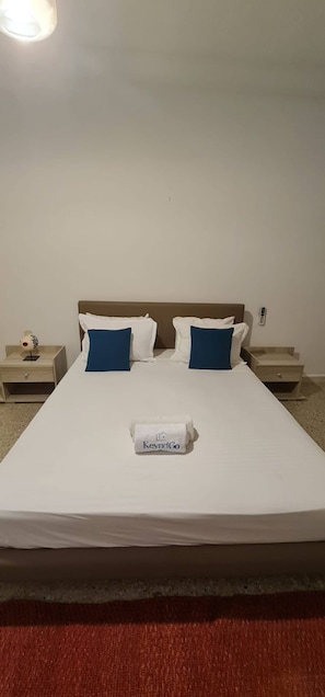 Quarto de hotel com uma cama grande, duas mesas de cabeceira e um telefone fixado na parede.