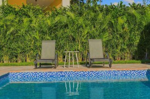 A swimming pool with two lounge chairs and a small table, surrounded by lush greenery. - 4BR Caribbean Villa in Hispaniola (Sosúa)