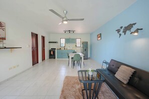 A living room with a sofa, a coffee table, and a dining area with chairs and a table. - Modern Sosua APT near beaches and cafe (Sosúa)