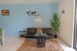 A living room with a sofa, a small table, a lamp, a world map on the wall, and a potted plant. - Modern Sosua APT near beaches and cafe (Sosúa)