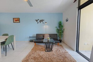 A living room with a sofa, a dining table with chairs, a small side table with a vase, a world map decoration, and a potted plant. - Modern Sosua APT near beaches and cafe (Sosúa)