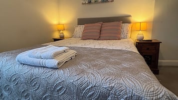 Un lit bien fait, avec une couvre-lit à motifs et des oreillers, deux lampes de chevet et une œuvre d’art accrochée au mur.