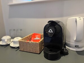 Una cafetera, una cesta con una caja roja y un electrodoméstico blanco sobre una encimera.