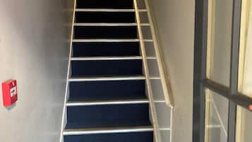 Un escalier avec une rampe, des marches recouvertes de moquette et un téléphone rouge pour les urgences fixé au mur.