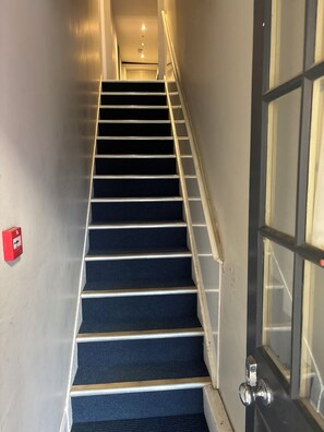 Una escalera con barandilla, escalones alfombrados y un teléfono rojo de emergencia en la pared.