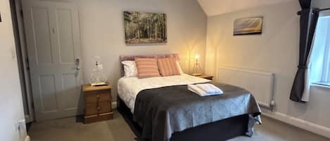 A bedroom with a bed, a nightstand, a dresser, a radiator, a door, and a window.