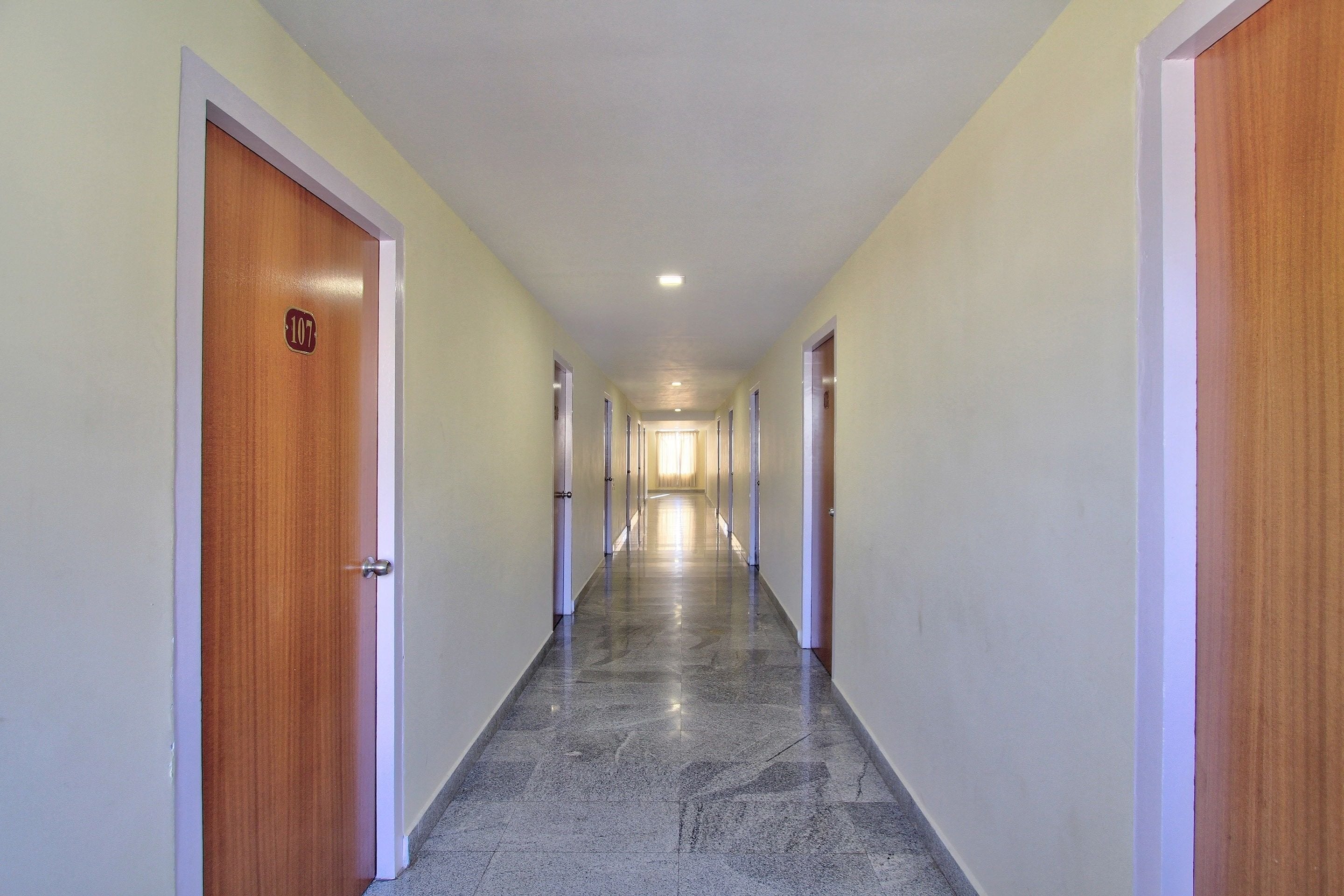 Un couloir avec des portes de chaque côté, un sol carrelé et un luminaire au plafond.