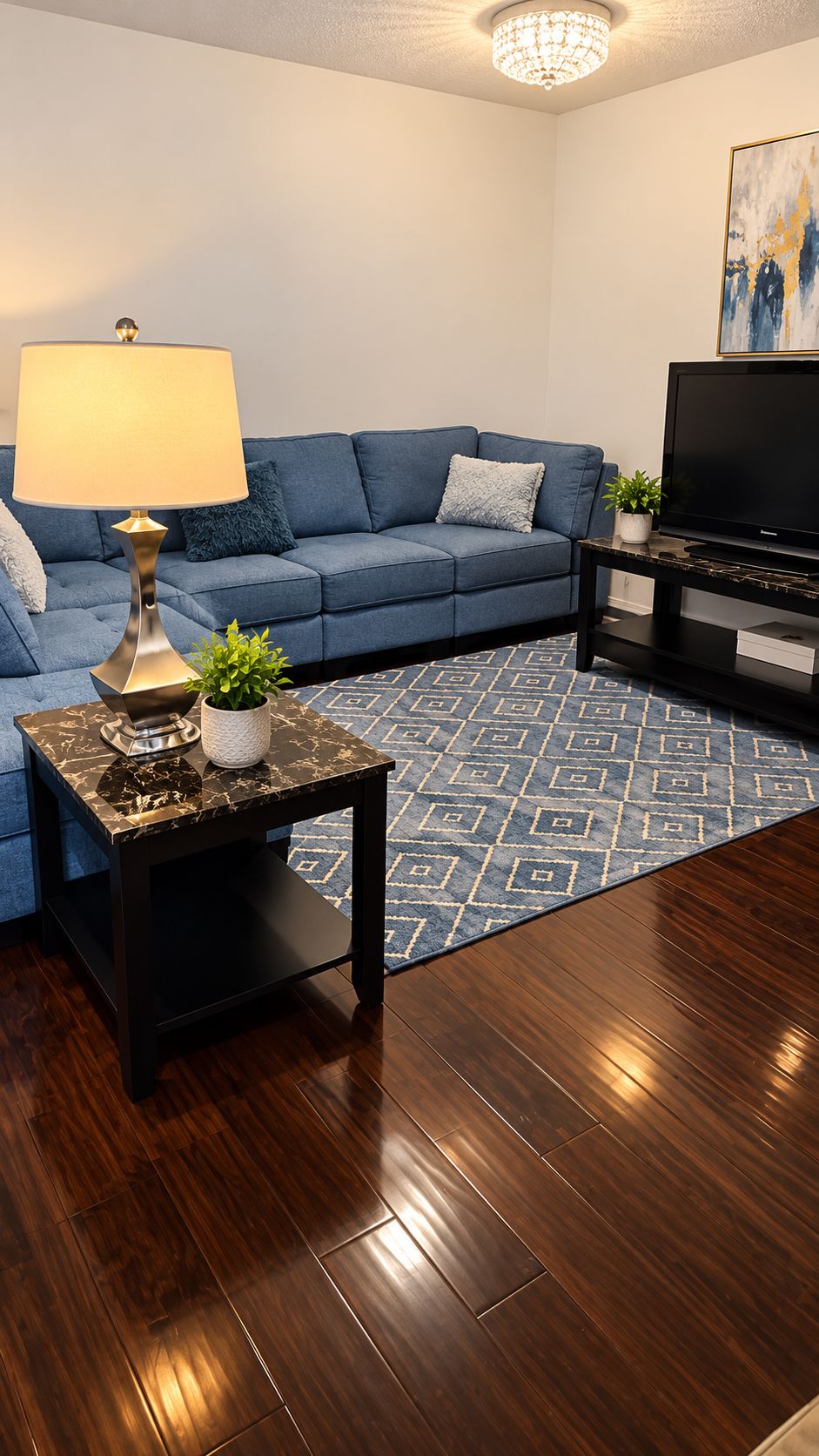 A modern living room with a blue sofa, a coffee table, a TV, and a patterned rug.
