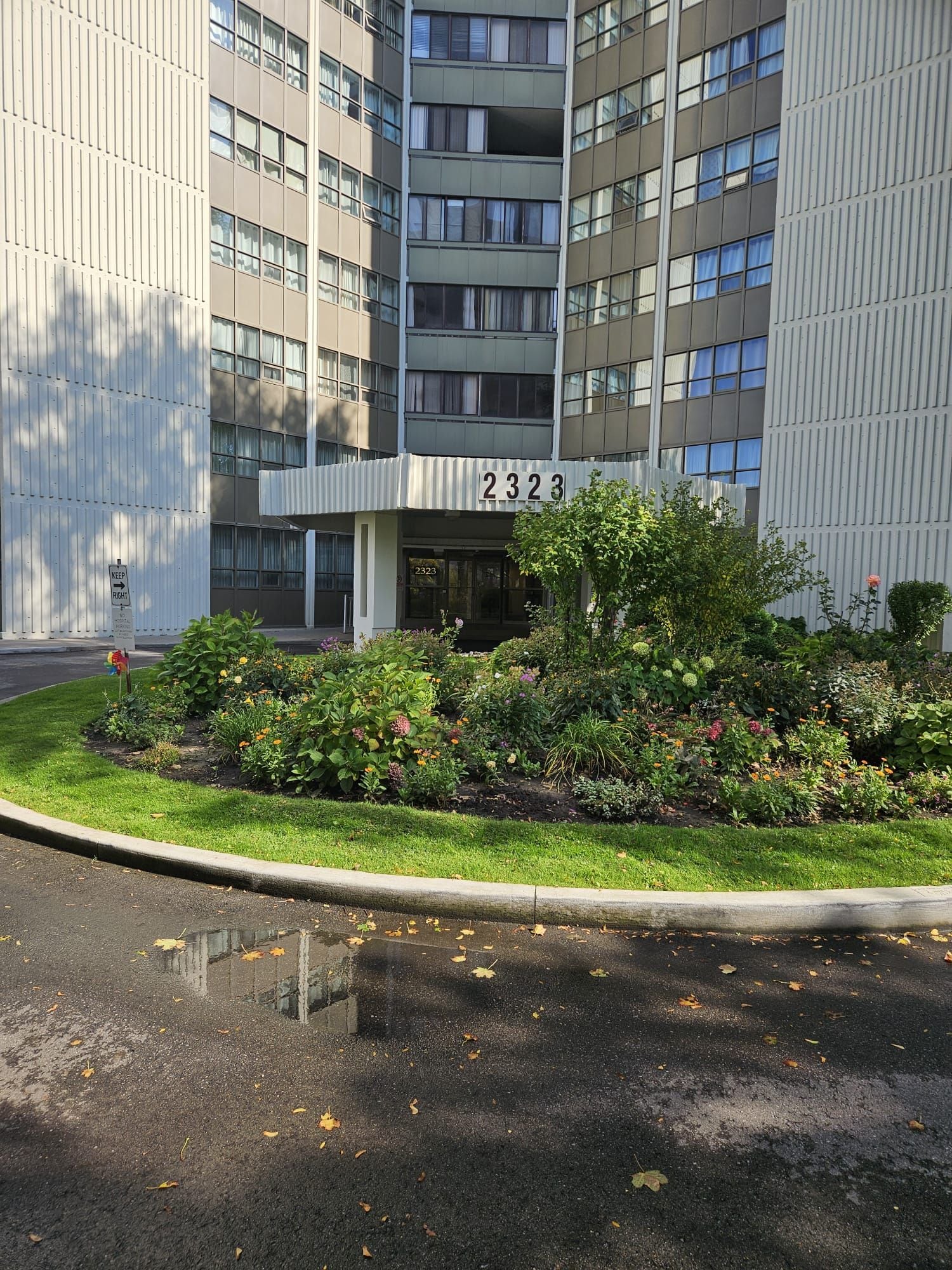 A multi-story building with a number 2323 sign, surrounded by a well-maintained garden with various plants and flowers.
