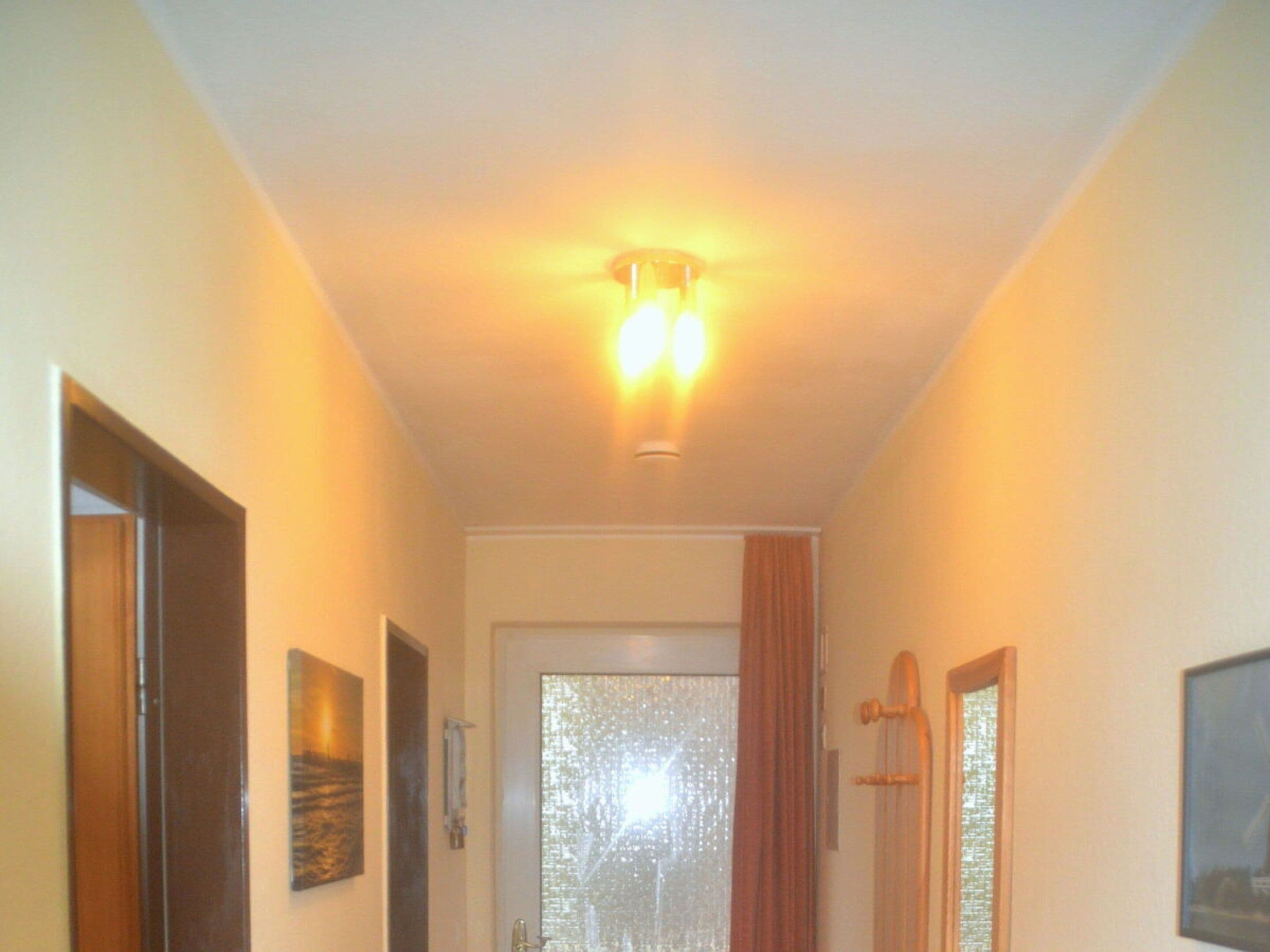 Ein Flur mit einer Tür am Ende, einer Leuchte darüber und einem Fenster mit Vorhängen.