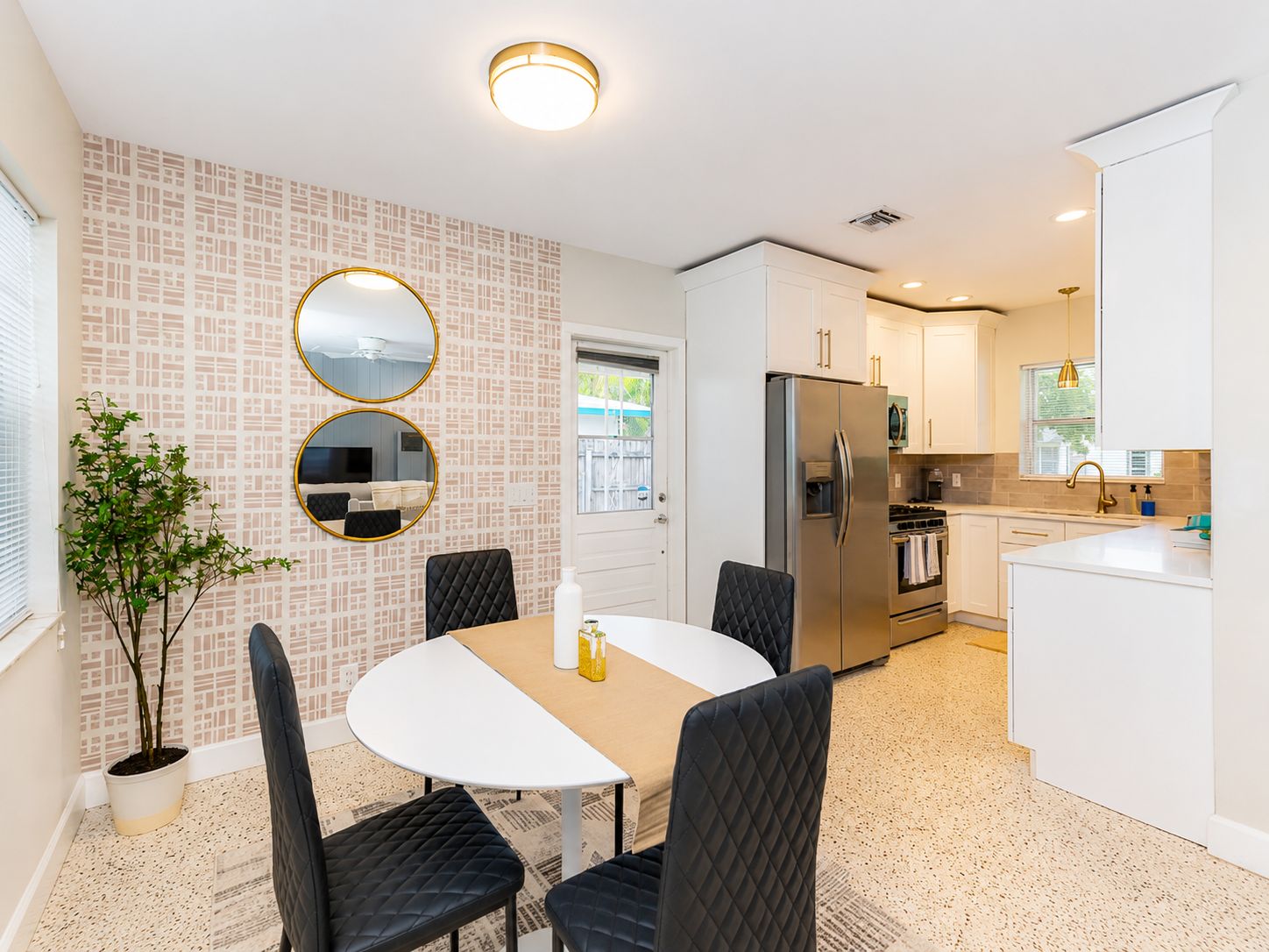 A modern kitchen with white cabinetry, a stainless steel refrigerator, and a dining area with a round table and black chairs.