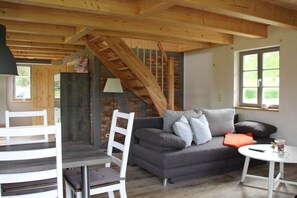 A cozy living room with a sofa, a dining table, and a chair. A staircase is visible in the background. - Holiday home with 2 bedrooms (Pelzkuhl OT Strasen)