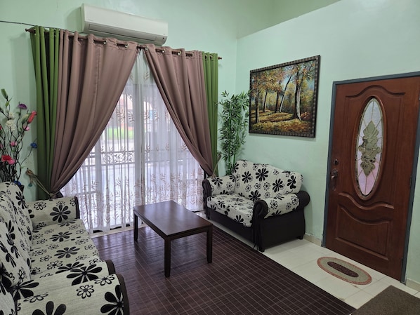 A living room with a sofa, a table, and a door with a decorative glass panel. - Sky Loft at Midhills Genting by HCK (Kuantan)