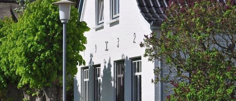 Un edificio blanco con el número '912' en su fachada, rodeado de vegetación y un farol.