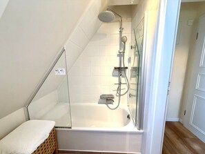 A modern bathroom with a glass-enclosed shower, a white bathtub, and a wooden bench. - "deichhof", No. 26 (Utersum)