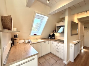 A compact kitchen with a skylight, white cabinetry, and a built-in microwave. - "deichhof", No. 26 (Utersum)