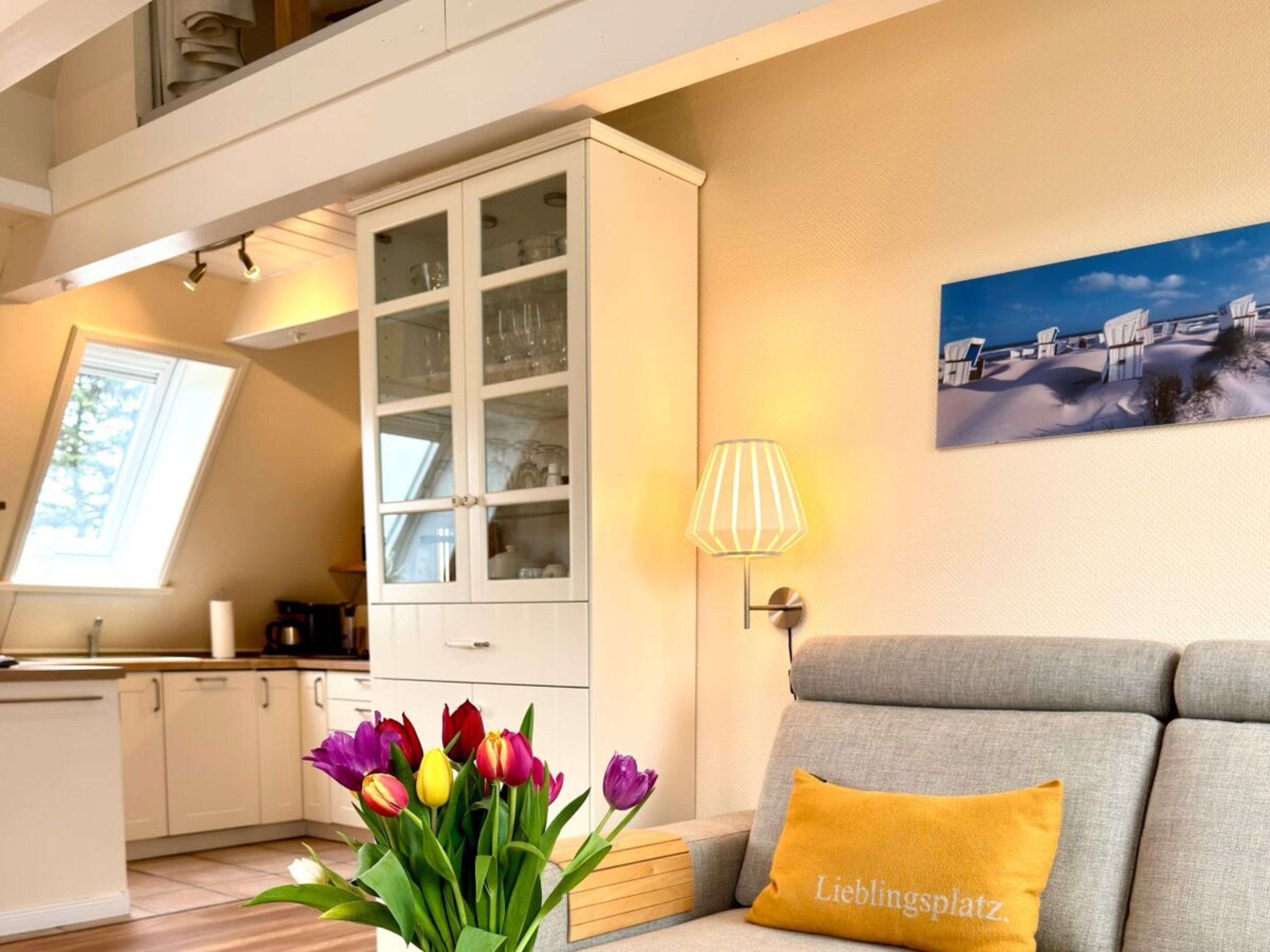 A modern kitchen with a built-in cabinet, a dining area with a grey sofa, and a painting on the wall.