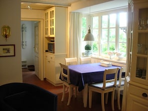 A dining area with a table set for four, white chairs, a window with a view of greenery, and a cabinet with glass doors. - Holiday Home at the spa Park 1a (Wyk auf Foehr)