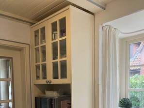 A room with a built-in cabinet with multiple glass doors, a window with curtains, and a small potted plant. - Holiday Home at the spa Park 1a (Wyk auf Foehr)