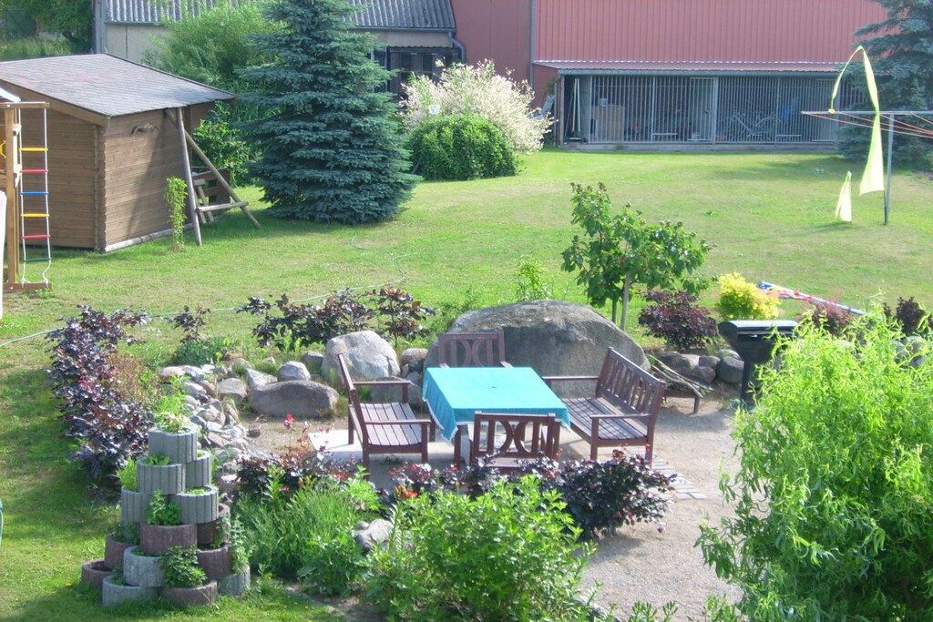 A garden with a wooden table and chairs, surrounded by rocks and plants.