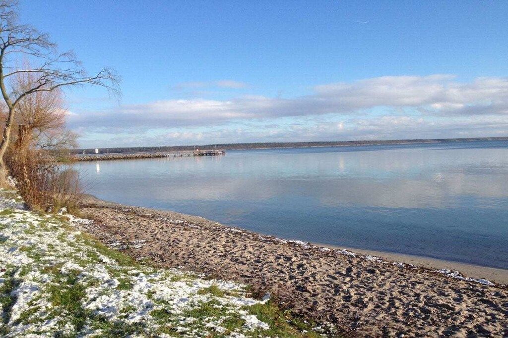 A calm lake with a dock extending into the water, surrounded by a rocky shoreline with patches of snow.