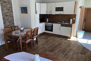Et kompakt køkken med hvide skabe, en træbordplade og et spiseområde med et bord og stole.