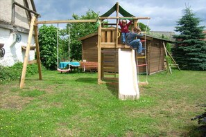 A wooden play structure with a slide and climbing elements in a grassy yard. - Müritz-Hof Knust - Farm (Klink \/ Sembzin)