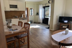 A kitchen with wooden cabinets, a dining table with chairs, a television, and a clock on the wall. - Müritz-Hof Knust - Farm (Klink \/ Sembzin)