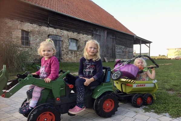 Three children on toy tractors in front of a rustic barn. - Müritz-Hof Knust - Farm (Klink \/ Sembzin)