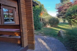Una cabana de fusta amb una finestra, un balcó de fusta i un camí de maó que condueix a un jardí.