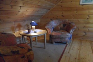 Habitació acollidora amb parets de fusta, una taula rodona amb una làmpada, un butac armchair estampat i una petita planta en test.