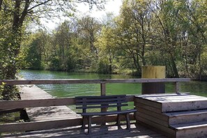 A wooden bench overlooking a calm river with trees in the background. - Holiday home in Rechlin with swimming pool (Rechlin)